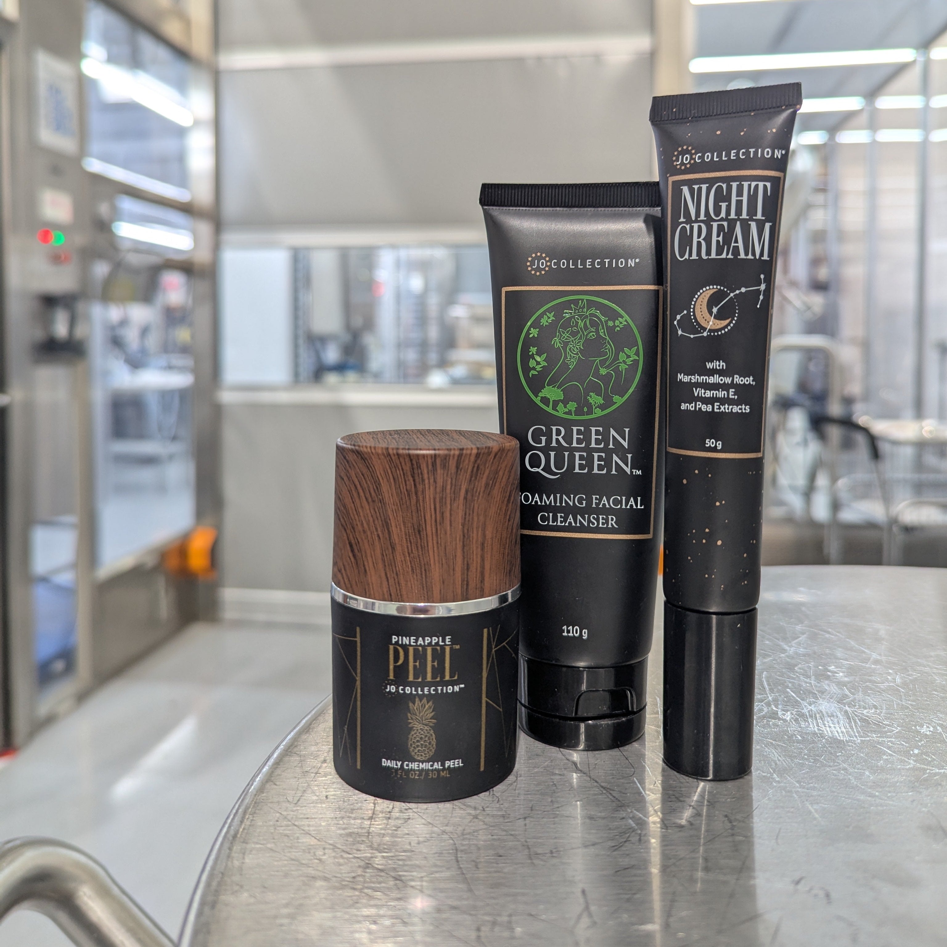 Three skincare products on a metallic surface with a blurred indoor background