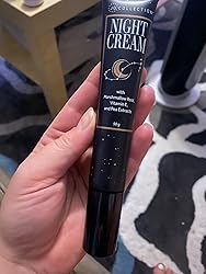 Hand holding a black tube of night cream with visible text.