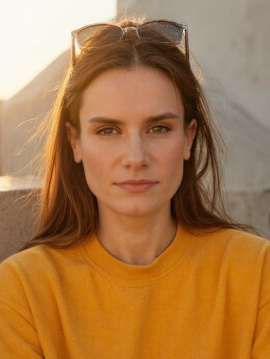 Leah Ward wearing a yellow shirt with sunglasses on her head, standing against a neutral background.