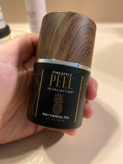 Hand holding a cylindrical product with 'Pineapple Peel' branding against a neutral background